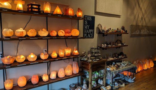 A cozy shop interior filled with various salt lamps and crystals displayed on wooden shelves.