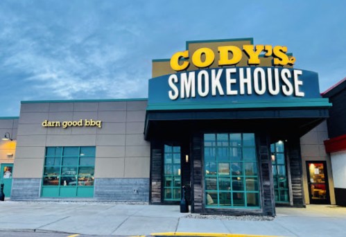 Exterior of Cody's Smokehouse restaurant, featuring a sign with "darn good BBQ" and a modern design at dusk.