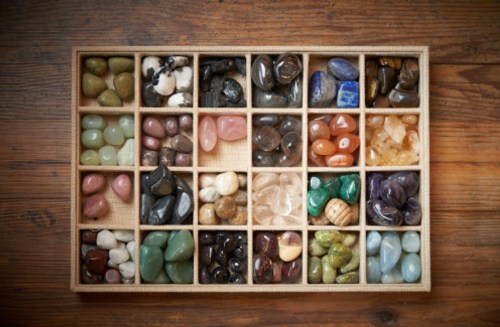 A wooden tray filled with various colorful gemstones arranged in small compartments.