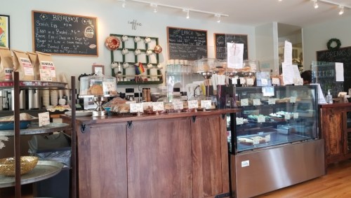 A cozy café interior featuring a wooden counter, display case with pastries, and a chalkboard menu.