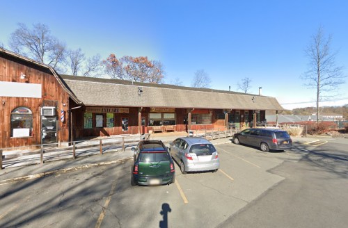 A rustic building with a wooden exterior, featuring parked cars in front and trees in the background under a clear blue sky.