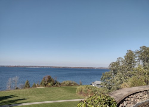 A serene view of a calm lake surrounded by greenery and a clear blue sky.
