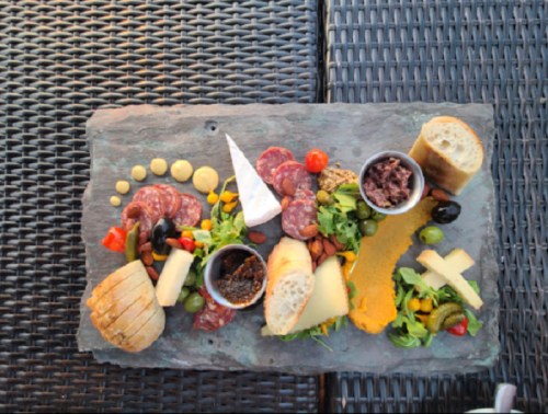 A charcuterie board featuring meats, cheeses, olives, bread, and condiments arranged on a slate platter.