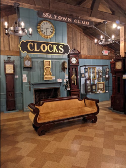 A cozy room featuring various antique clocks, a wooden bench, and rustic decor under a wooden ceiling.