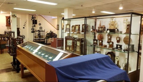 A museum display featuring various antique clocks and timepieces in glass cases and on shelves.