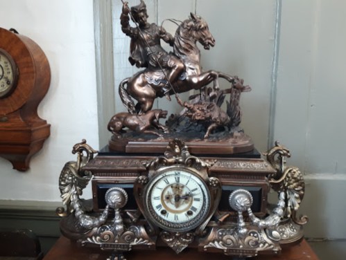 A vintage clock with a bronze statue of a cowboy on horseback, surrounded by ornate decorative elements.