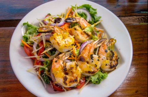 A vibrant salad topped with grilled shrimp, mixed greens, tomatoes, and shredded vegetables on a white plate.