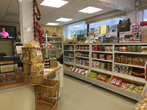 A cozy store interior with shelves of various packaged foods, snacks, and kitchen items, plus a TV in the background.