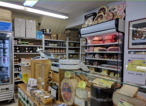 A cozy cheese shop interior featuring shelves of cheeses, meats, and gourmet products, with a display case in the center.
