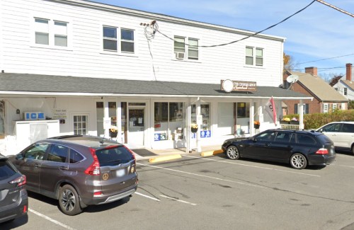 A small commercial building with multiple storefronts, parked cars, and a clear blue sky.