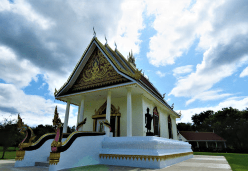 A beautifully ornate temple with intricate gold details, set against a cloudy sky and surrounded by greenery.