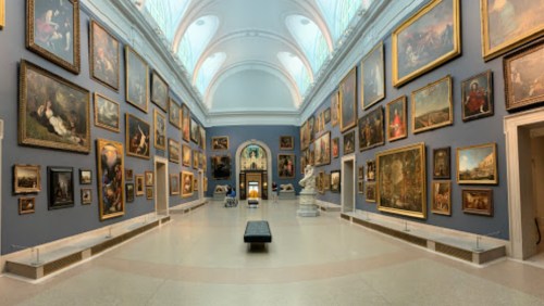 A spacious art gallery with numerous framed paintings on the walls and a central bench for visitors.