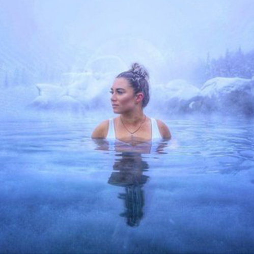 A woman with a bun is partially submerged in a misty, serene blue water landscape.