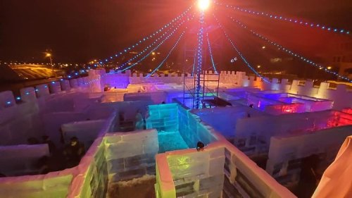 A colorful ice castle at night, illuminated with lights, featuring maze-like structures and a central tower.