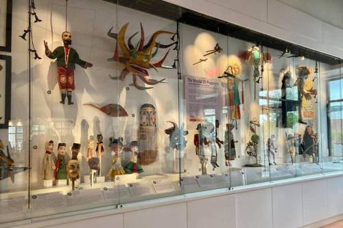 A display of colorful puppets and masks in a glass case, showcasing various cultural artifacts.