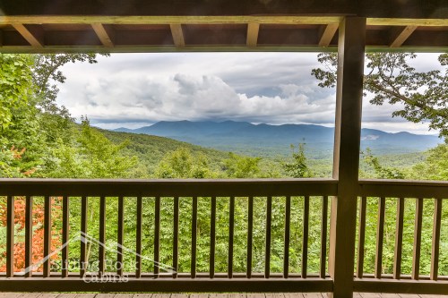 Scenic mountain view from a cabin porch, surrounded by lush greenery and cloudy skies.