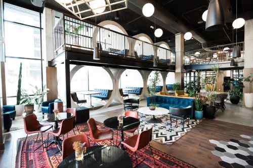 Modern lounge area with colorful seating, plants, and large windows, featuring a mix of textures and patterns.