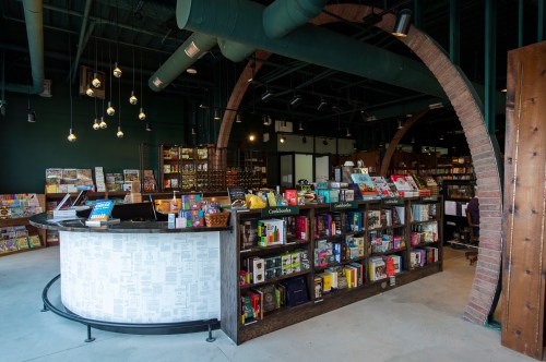 A modern bookstore interior featuring a curved counter and shelves filled with colorful books under warm lighting.