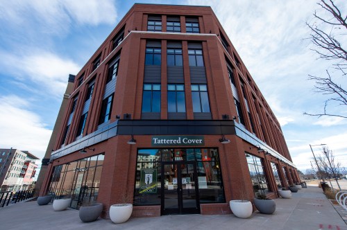 A modern brick building with large windows, featuring the entrance of Tattered Cover bookstore.