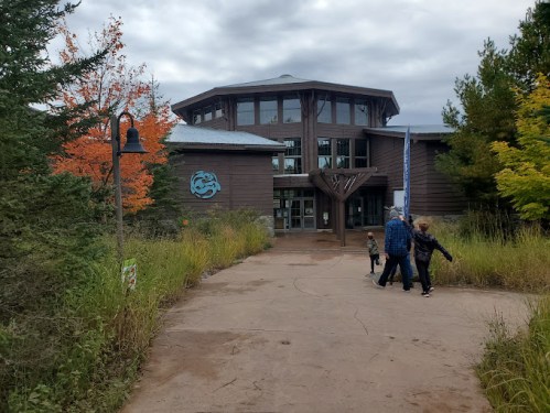 A modern building surrounded by trees and colorful foliage, with people walking towards the entrance on a path.