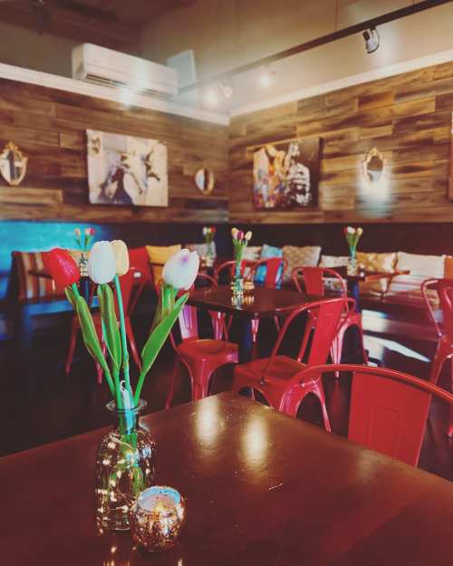 A cozy restaurant interior with wooden walls, red chairs, and tables adorned with tulips and a candle.