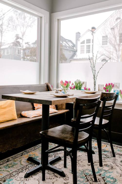 Cozy dining area with a wooden table, chairs, and a window view of tulips outside. Soft colors and a welcoming atmosphere.