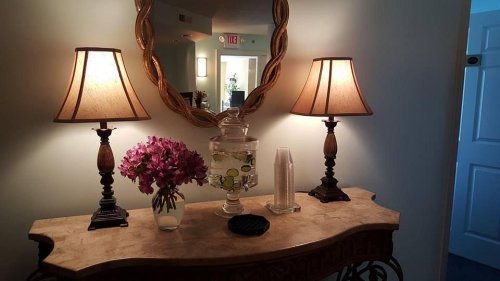 A decorative console table with two lamps, a floral arrangement, and a glass jar filled with water and lemon slices.