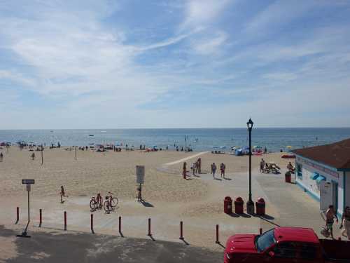 A sunny beach scene with people enjoying the sand and water, umbrellas, and a clear blue sky.