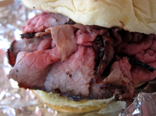 Close-up of a sandwich filled with tender, sliced roast beef on a soft bun, wrapped in foil.