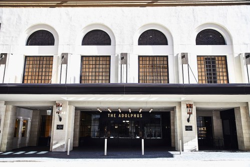 Exterior view of The Adolphus hotel, featuring arched windows and a modern entrance.