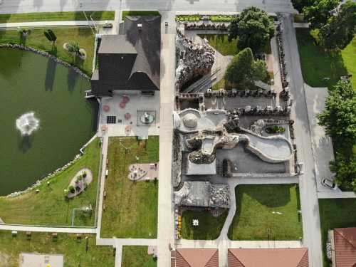 Aerial view of a unique stone structure beside a pond, surrounded by landscaped gardens and pathways.