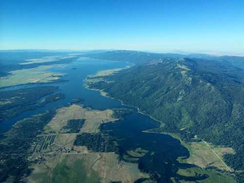 Aerial view of a vast lake surrounded by green hills and farmland under a clear blue sky.