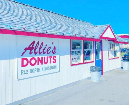 A bright exterior of Allie's Donuts shop with a sign and a blue door, set against a clear blue sky.