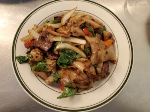 A plate of stir-fried noodles with beef, vegetables, and herbs, garnished with onions and colorful peppers.
