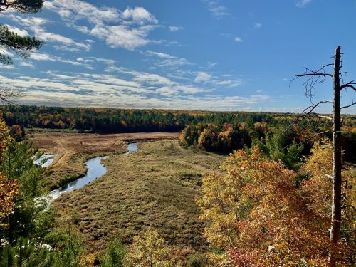A scenic view of a river winding through a colorful autumn landscape with trees and a blue sky.