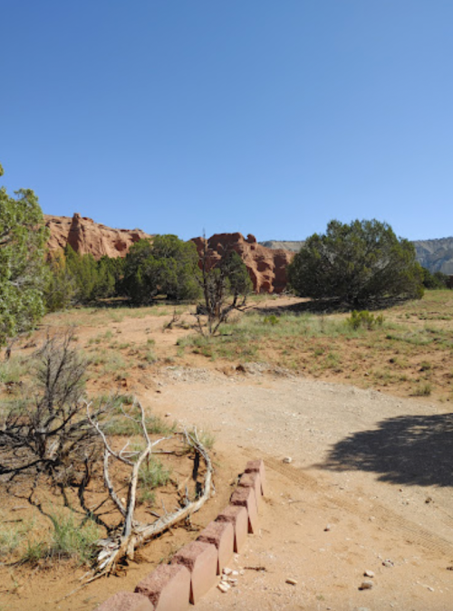 A dirt path leads through a desert landscape with sparse vegetation and rocky formations under a clear blue sky.