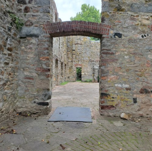A stone ruin with an archway leading to a grassy area, surrounded by weathered walls and a cobblestone floor.