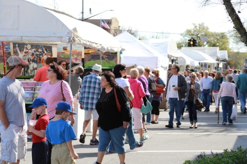 A bustling outdoor market with people browsing tents and stalls, enjoying a sunny day.