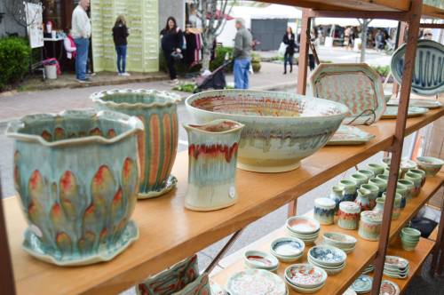 A display of colorful handmade pottery on wooden shelves at an outdoor market.