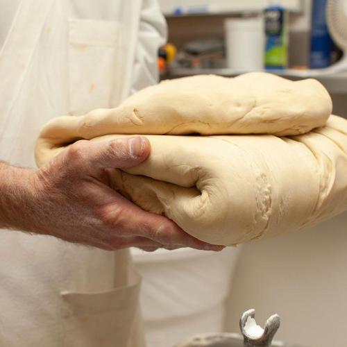 A hand holding a large, smooth, folded piece of dough in a kitchen setting.