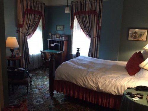 Cozy bedroom with a large bed, patterned curtains, a desk, and warm lighting.