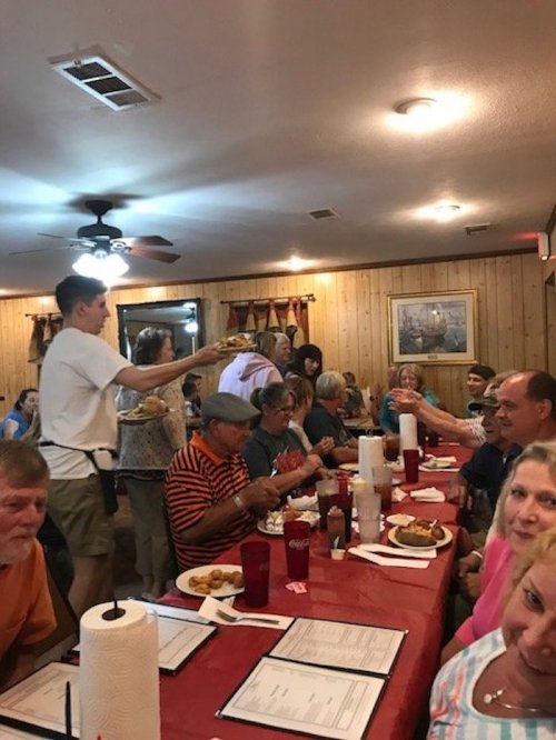 A busy restaurant scene with diners at tables, a server delivering food, and a warm, inviting atmosphere.