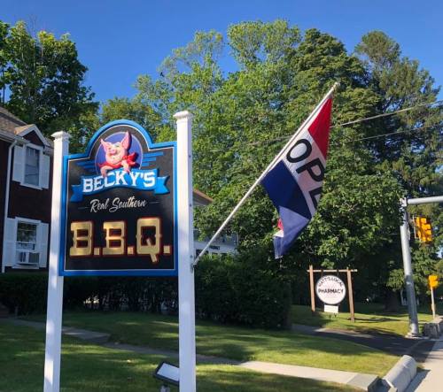 Sign for Becky's Real Southern BBQ with an "Open" flag in front of a green landscape.
