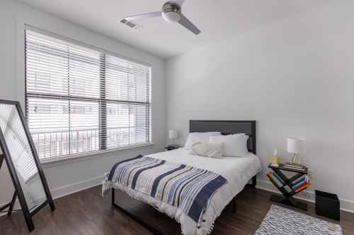 A modern bedroom with a bed, striped blanket, nightstands, and large window with blinds.