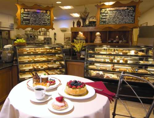 A cozy café display with a table featuring desserts and coffee, surrounded by glass cases of pastries and a menu board.