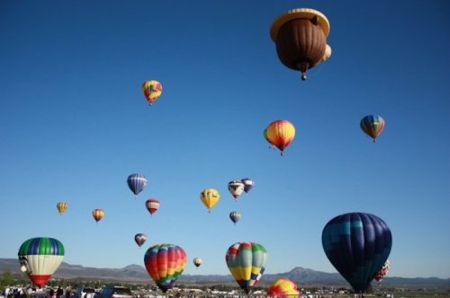 A vibrant sky filled with colorful hot air balloons, with a clear blue backdrop and spectators below.