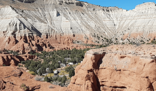 A scenic view of layered rock formations and a lush valley with small buildings nestled among the greenery.