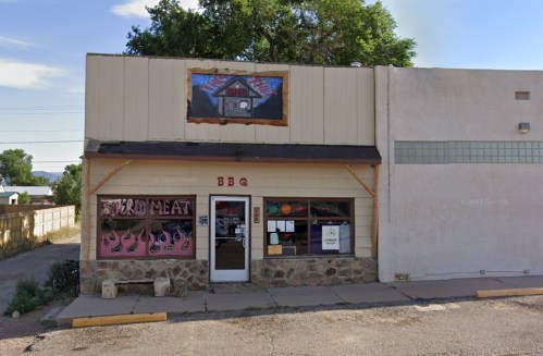 A small BBQ restaurant with a stone facade and colorful signage, featuring a "Smoked Meat" display in the window.