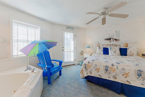 Cozy beach-themed bedroom with a large bed, blue chair, and a small umbrella by the door. Bright and inviting atmosphere.