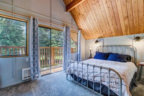 Cozy bedroom with a metal bed frame, large windows, and wooden ceiling, overlooking a green outdoor space.